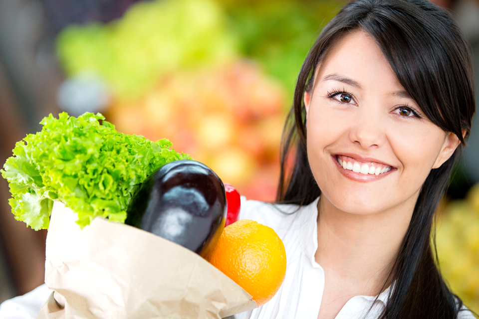Asian woman looking happy while holding up a grocery bag full of vegetables